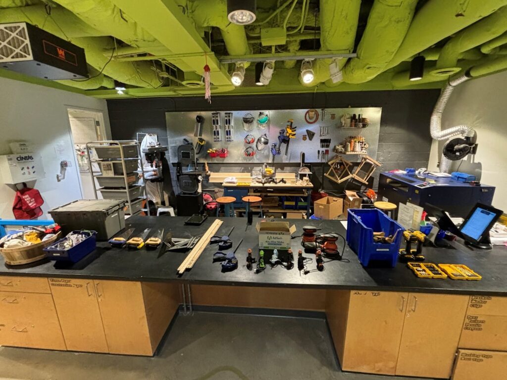 Large workshop showing a table and walls full of wordworking tools such as saws, drills, sanders, glue guns, clamps, and safety gear.
